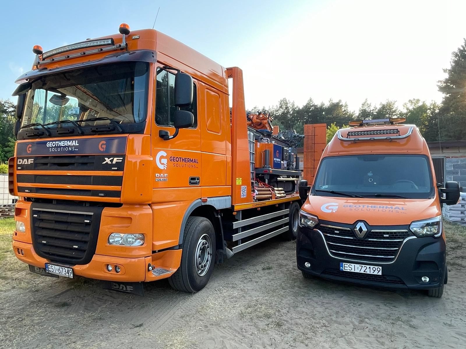 Pomarańczowa ciężarówka DAF XF i bus Renault Master z logo firmy w branży geotermalnej, zaparkowane na placu budowy.