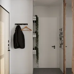 Minimalistyczny przedpokój z drewnianymi akcentami: płaszcz na wieszaku, pionowa donica z rośliną pnącą, drzwi z okleiną drewnopodobną i rama z surowego drewna.