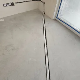 Wnętrze w trakcie remontu: kable elektryczne prowadzone w bruzdach w ścianie i podłodze, puszki elektryczne w ścianie, okno zabezpieczone taśmą malarską.