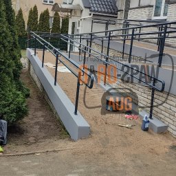 DARO-SPAW AUG DARIUSZ HOŁUBOWICZ - Rampa dla niepełnosprawnych z metalowymi poręczami przy budynku, widoczne narzędzia i puszka farby, teren po budowie.