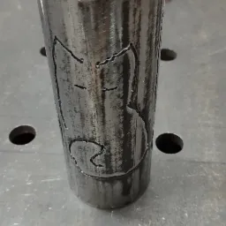 Metalowa rura z wyciętym laserowo wzorem przedstawiającym postać z kreskówki, leżąca na metalowym stole warsztatowym.