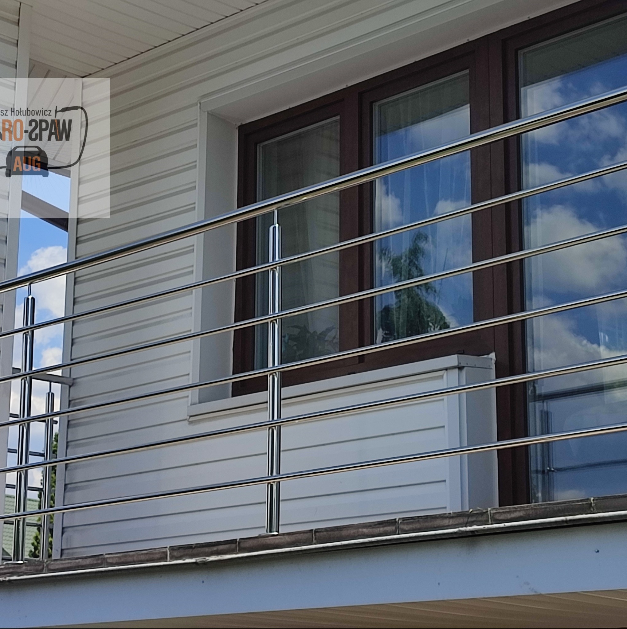 Barierka balkonowa ze stali nierdzewnej z widocznym odbiciem nieba i chmur w oknach i na powierzchni metalu.