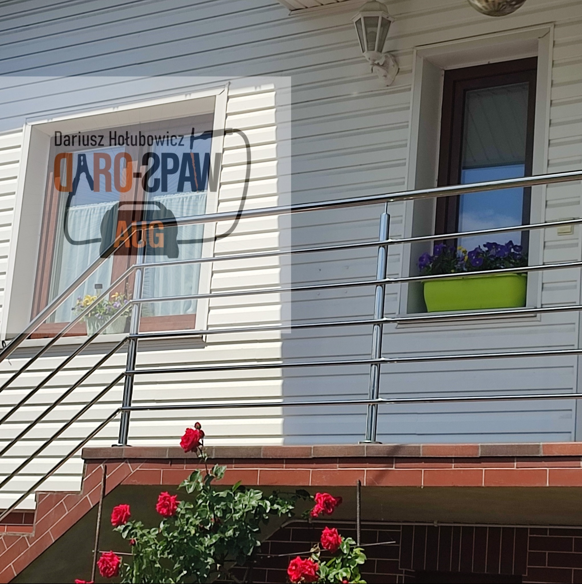 Metalowa balustrada schodowa z poziomymi prętami, widok na elewację domu z oknami i kwiatami, krzew róż na pierwszym planie.