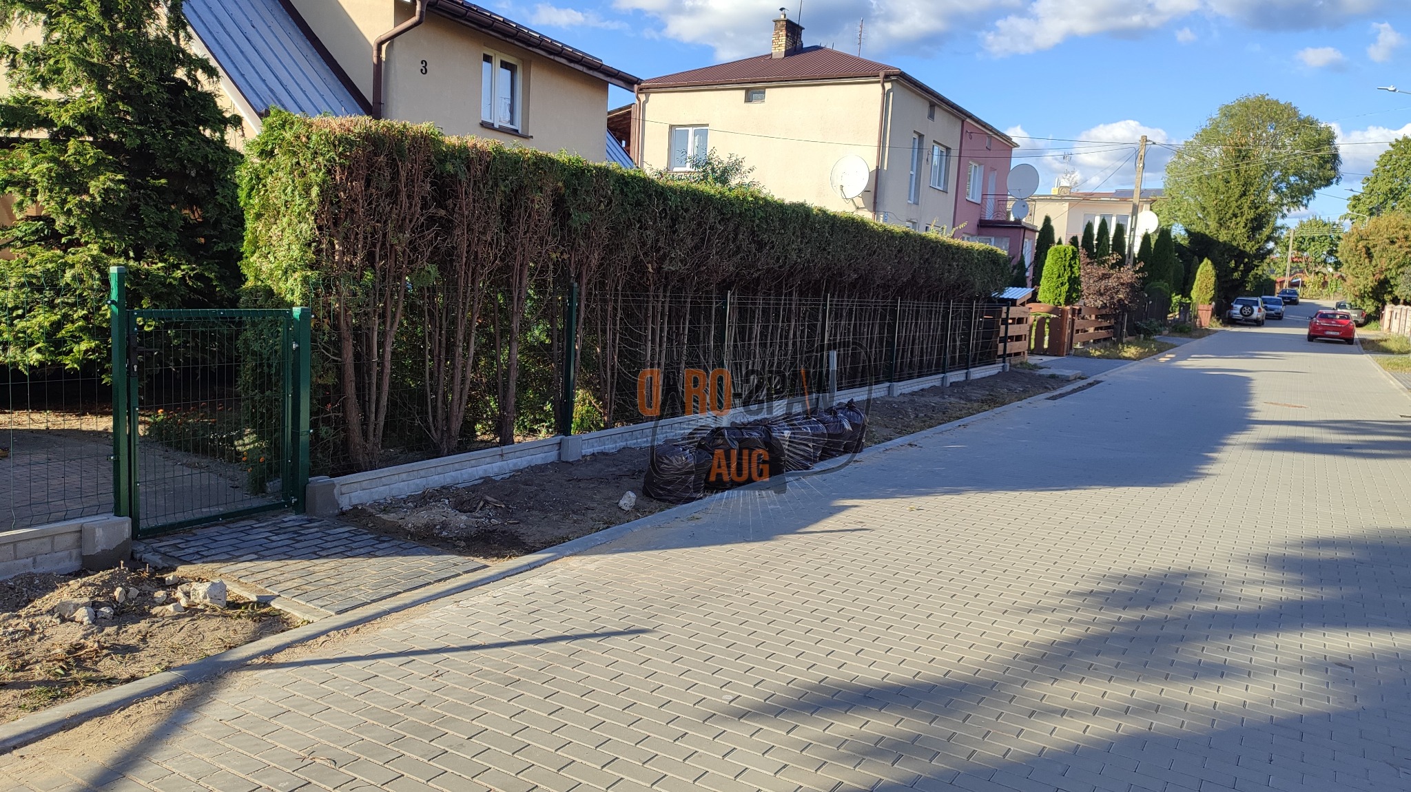 Fragment posesji z nowym ogrodzeniem panelowym z podmurówką, widoczne czarne worki z ziemią wzdłuż chodnika