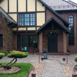 EKTA OGRÓD - Czyszczenie elewacji domu z czerwonej cegły za pomocą myjki ciśnieniowej, widoczne zarośnięte pnącza na ścianach i zadbany ogród z ozdobnymi krzewami.