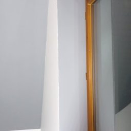 EKTA OGRÓD - Świeżo pomalowane wnętrze z szarą ścianą i białym sufitem, widoczna drewniana rama okienna po prawej stronie.