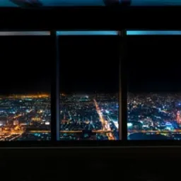 Panoramiczny widok na nocne miasto przez duże okna z wąskimi ramami, widoczna perspektywa ulic i świateł miejskich z góry.