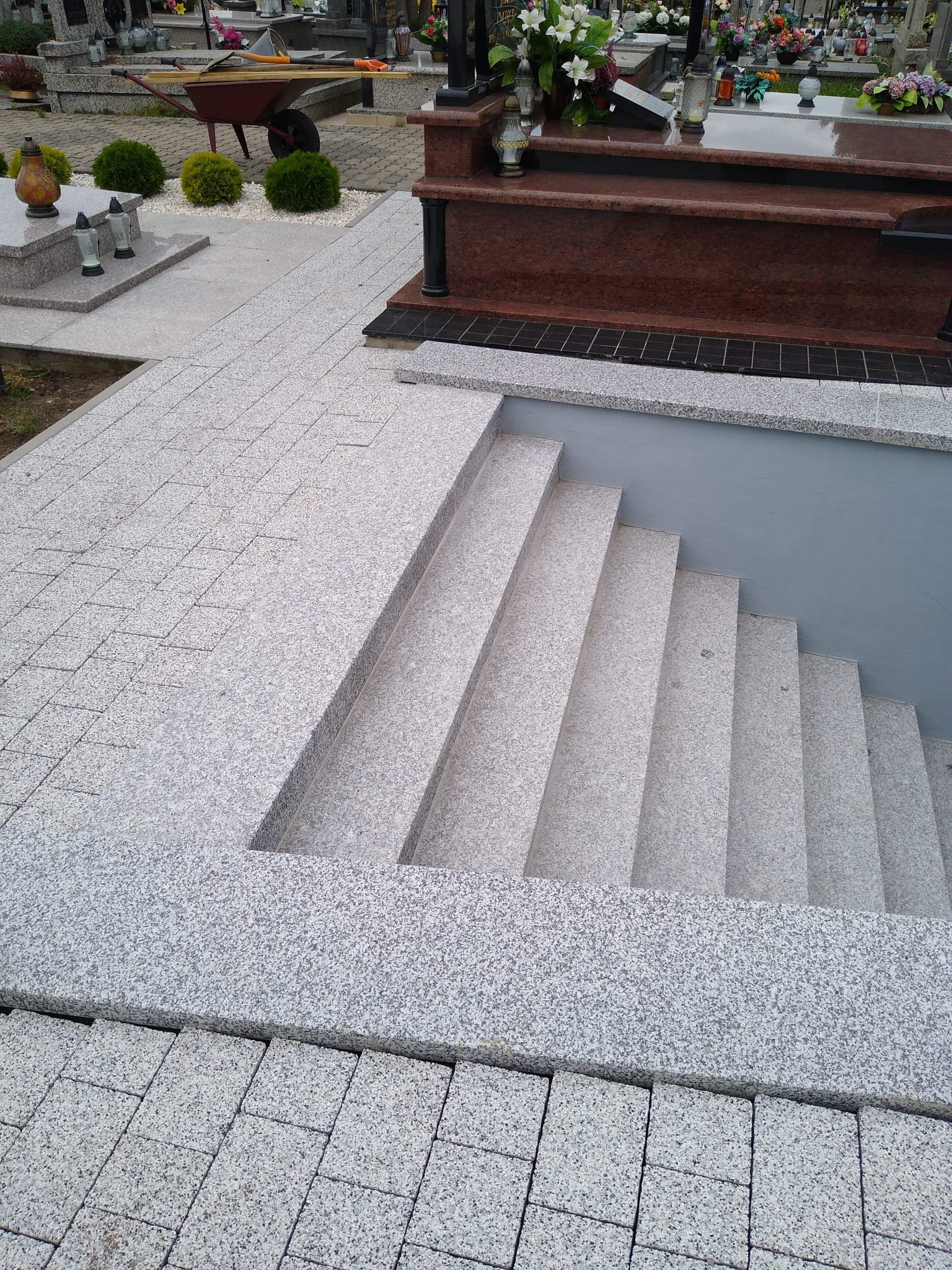 Granitowe schody prowadzące do piwnicy grobowca, otoczone kostką granitową i widocznym nagrobkiem w tle.