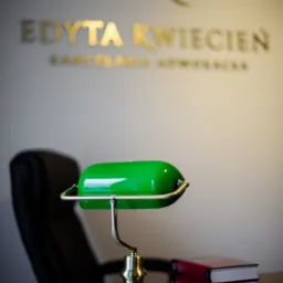 Gabinet z biurkiem, lampką bankierską, wizytówką i książkami, na ścianie logo 'EK' i nazwa 'Edyta Kwiecień Kancelaria Adwokacka'.