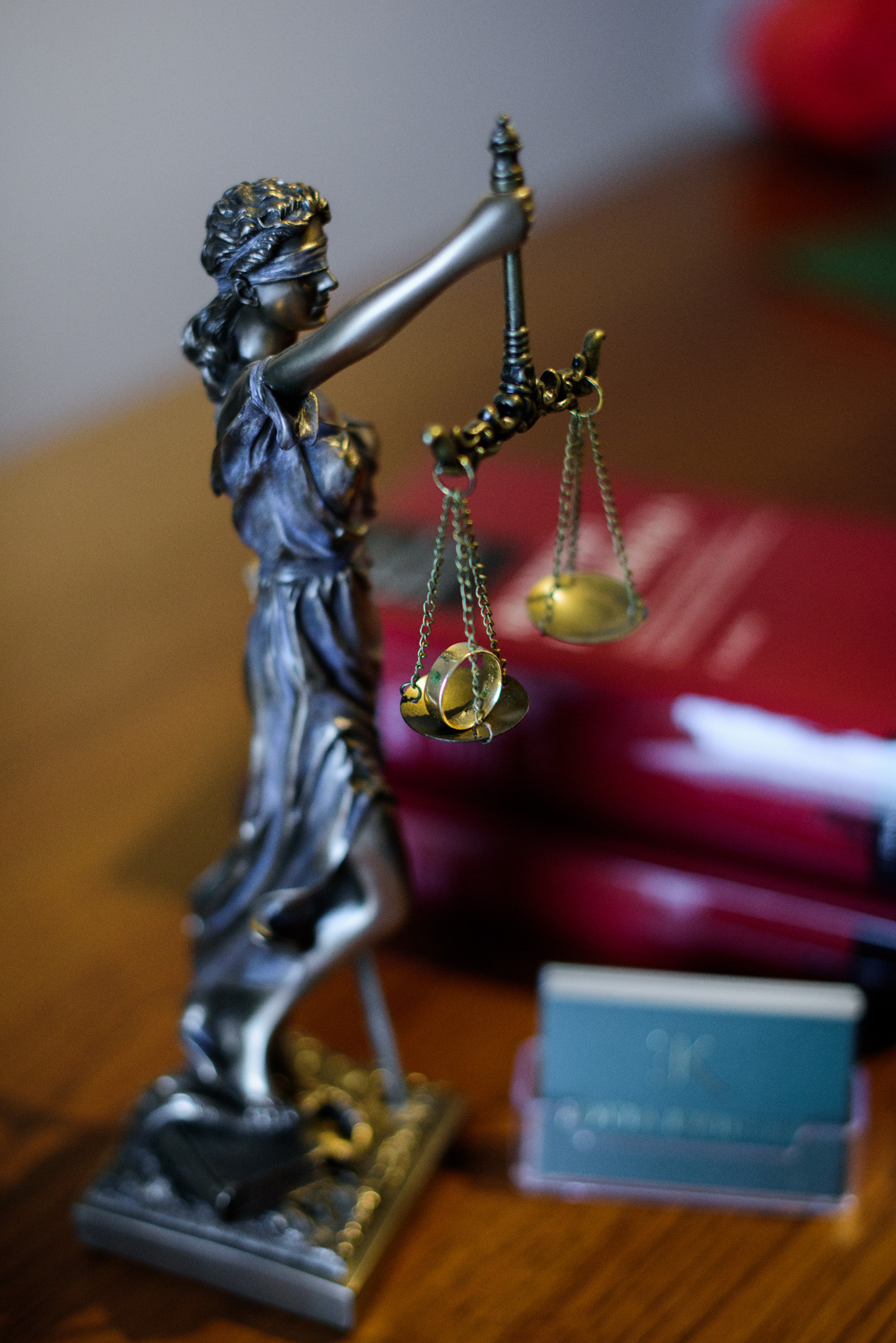 Statuetka Temidy z wagą, na której zawieszone są obrączki ślubne, w tle książki i wizytownik.