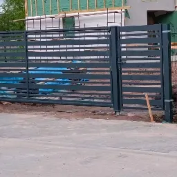 Nowoczesna, pozioma brama wjazdowa z metalowymi profilami, z widocznymi elementami montażowymi i fragmentem ogrodzenia z siatki na posesji w trakcie budowy.