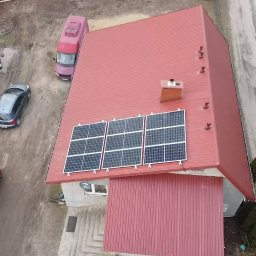 Marek Stryjewski - Widok z góry na dom z czerwonym dachem, na którym zamontowane są trzy panele fotowoltaiczne; obok domu zaparkowane samochody.