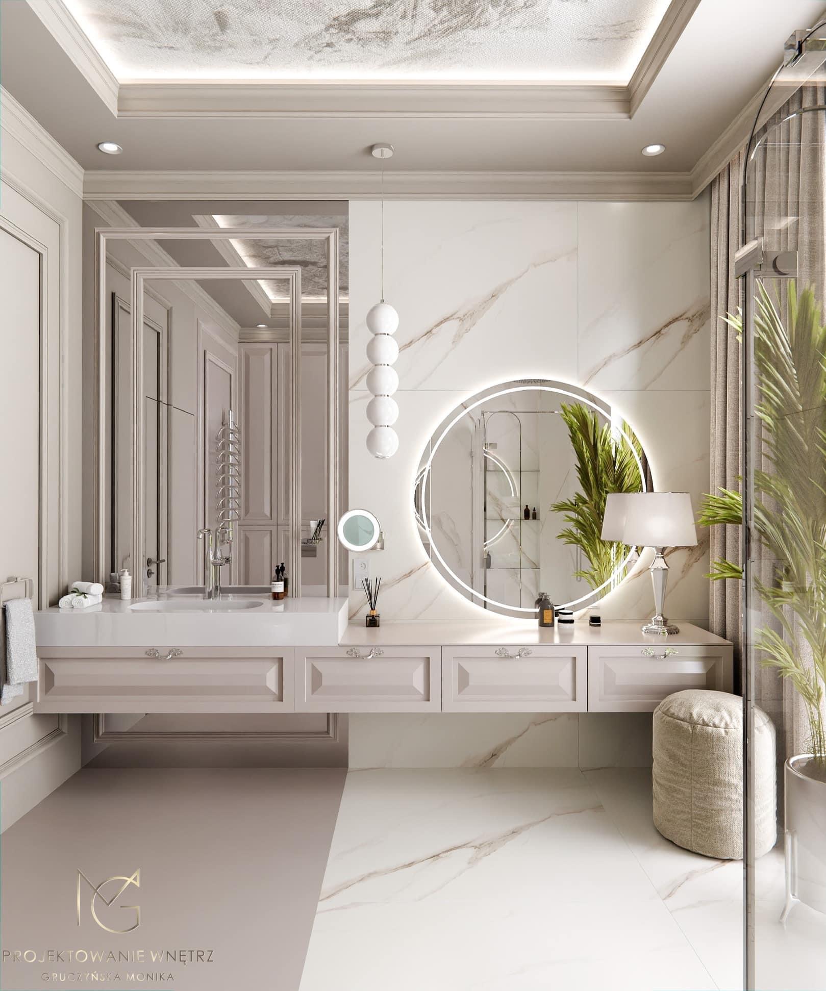Elegancka łazienka w odcieniach beżu i bieli z marmurowymi akcentami, okrągłym lustrem z podświetleniem LED, wiszącą szafką z umywalką i dekoracyjną lampą stołową, widok na kabinę prysznicową...