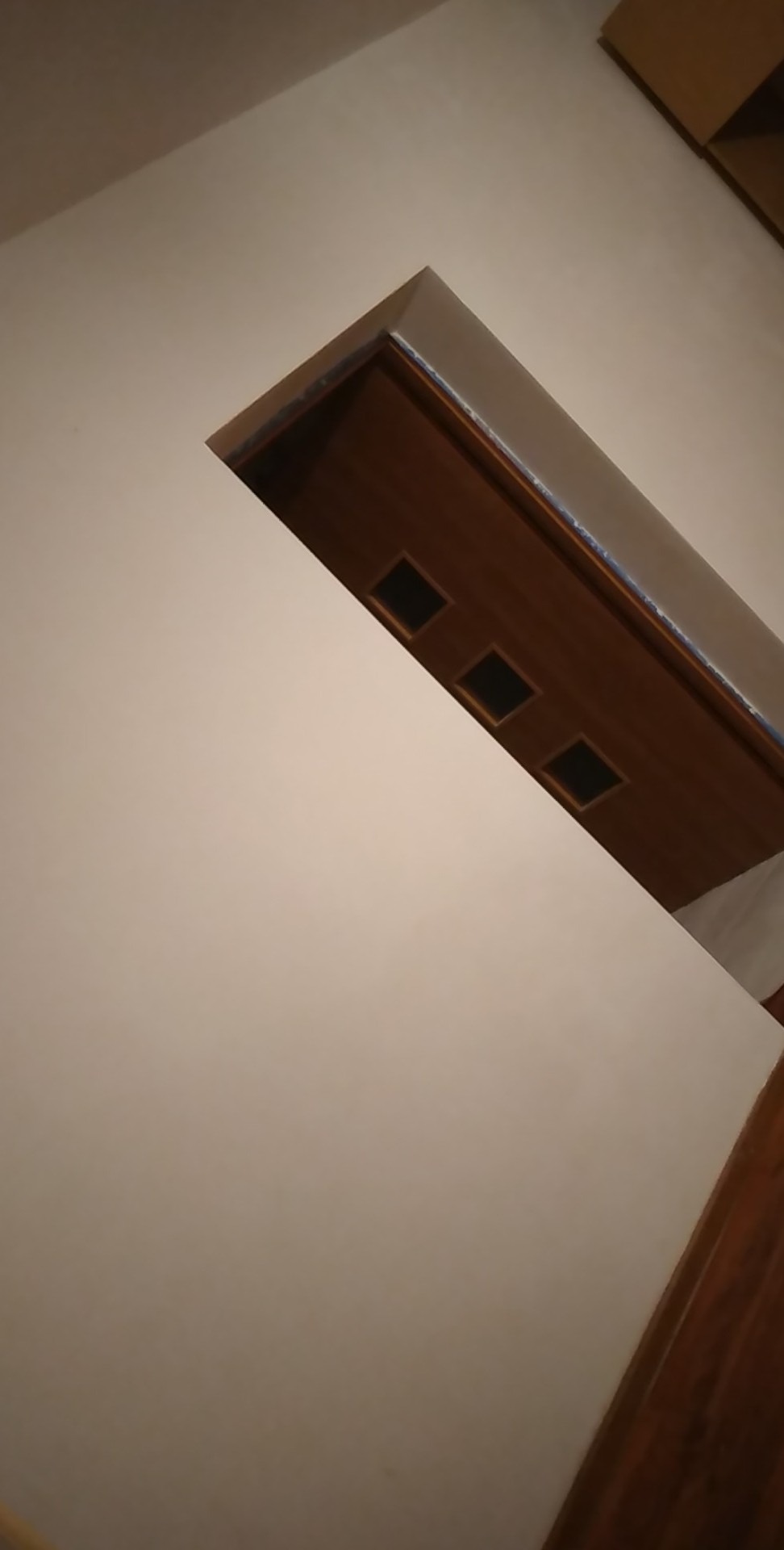 Świeżo pomalowana, jasna ściana z widocznym fragmentem drewnianych drzwi z trzema kwadratowymi wgłębieniami, ujęcie pod kątem.