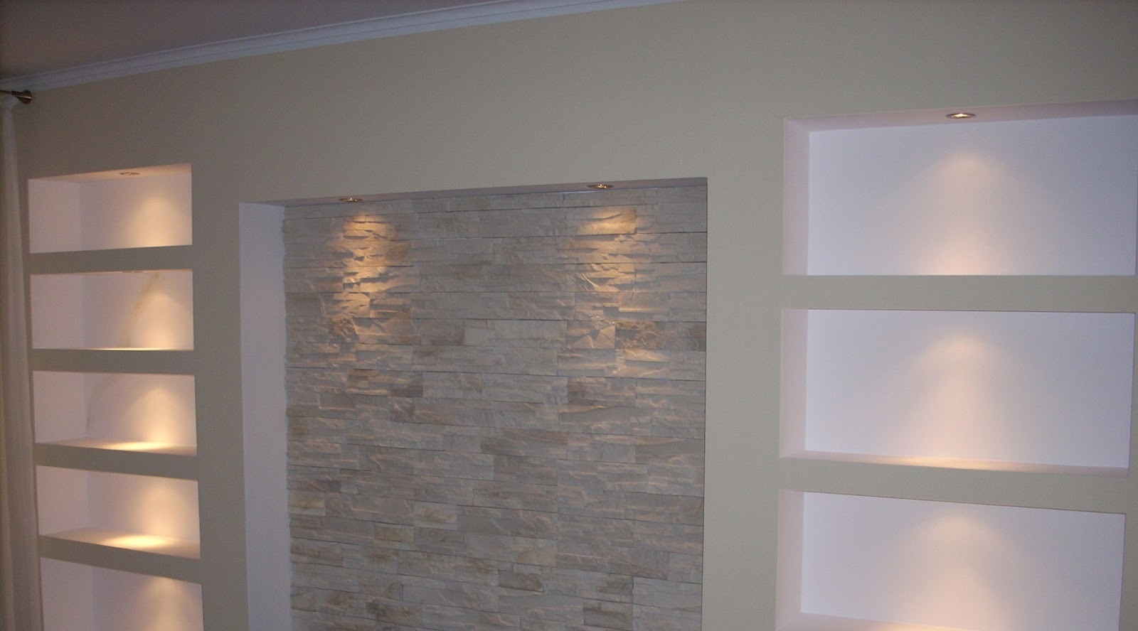 Ściana z dekoracyjną okładziną kamienną i podświetlanymi wnękami w jasnym wnętrzu.