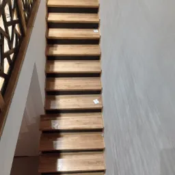 Drewniane schody z ażurową balustradą, widok z dołu, ściana z efektem dekoracyjnym.