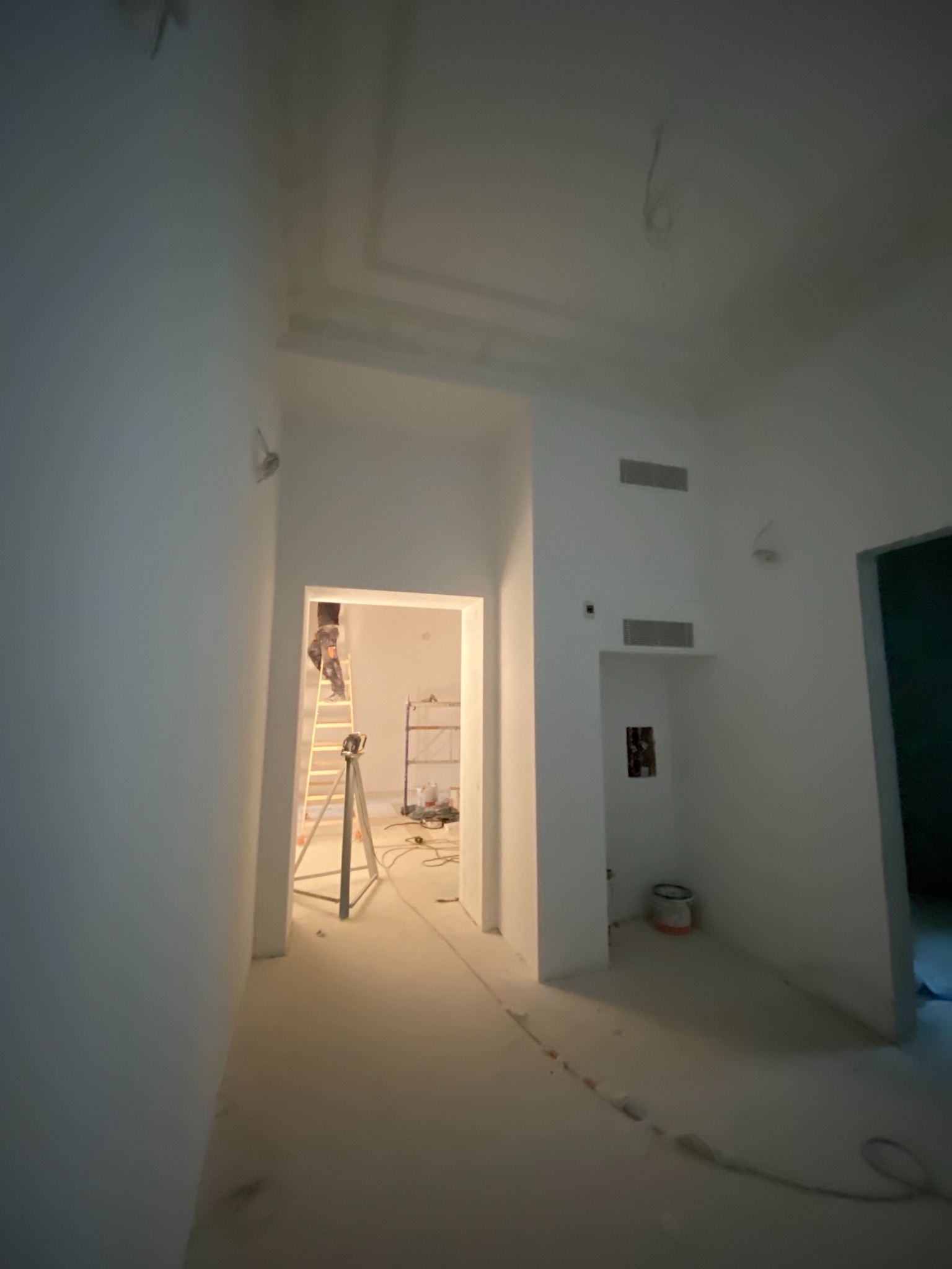 Prace malarskie w trakcie realizacji w Rząśniku: malarz na drabinie w jasnym wnętrzu, widoczne przygotowania i narzędzia malarskie.