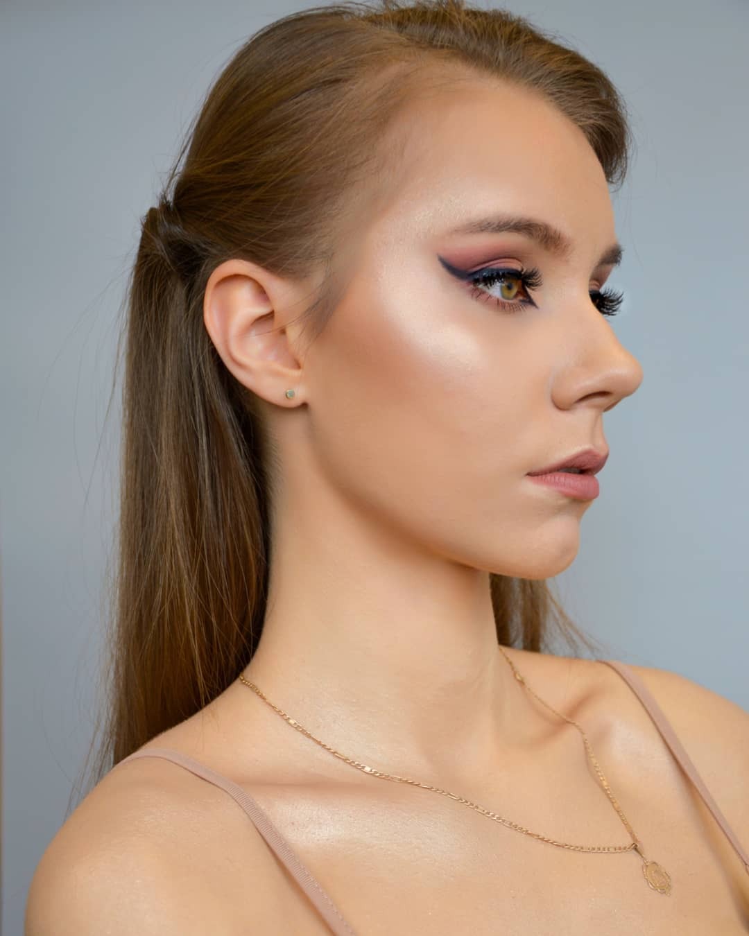 Portret kobiety z profesjonalnie wykonanym, wieczorowym lookiem, z wyraźnie podkreślonym okiem eyelinerem w kolorze czarnym z fioletowym cieniem i rozświetlonym policzkiem, w minimalistycznej...