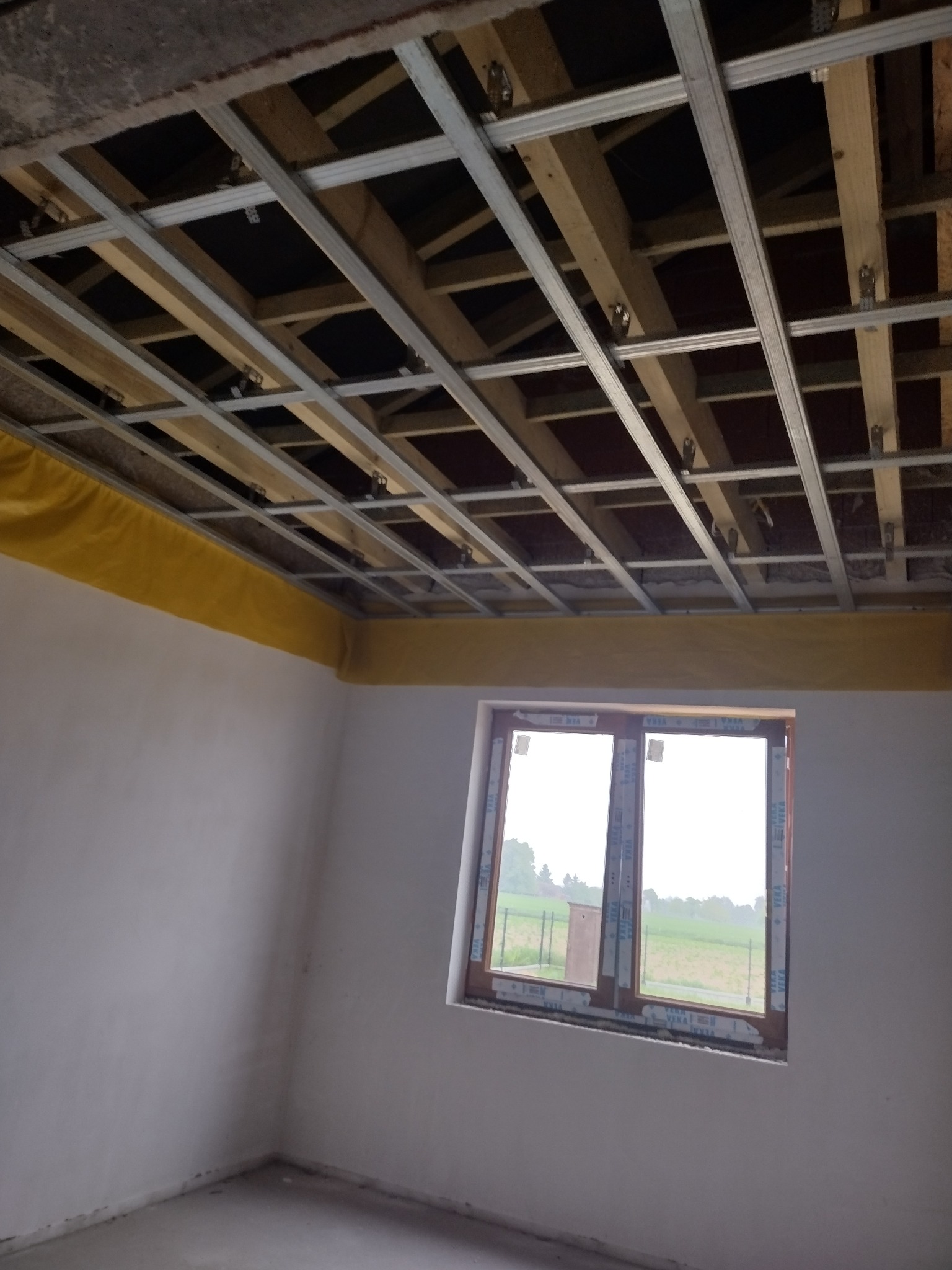 Stelaż sufitu podwieszanego z izolacją z wełny mineralnej, widok na okno z widokiem na zewnątrz.