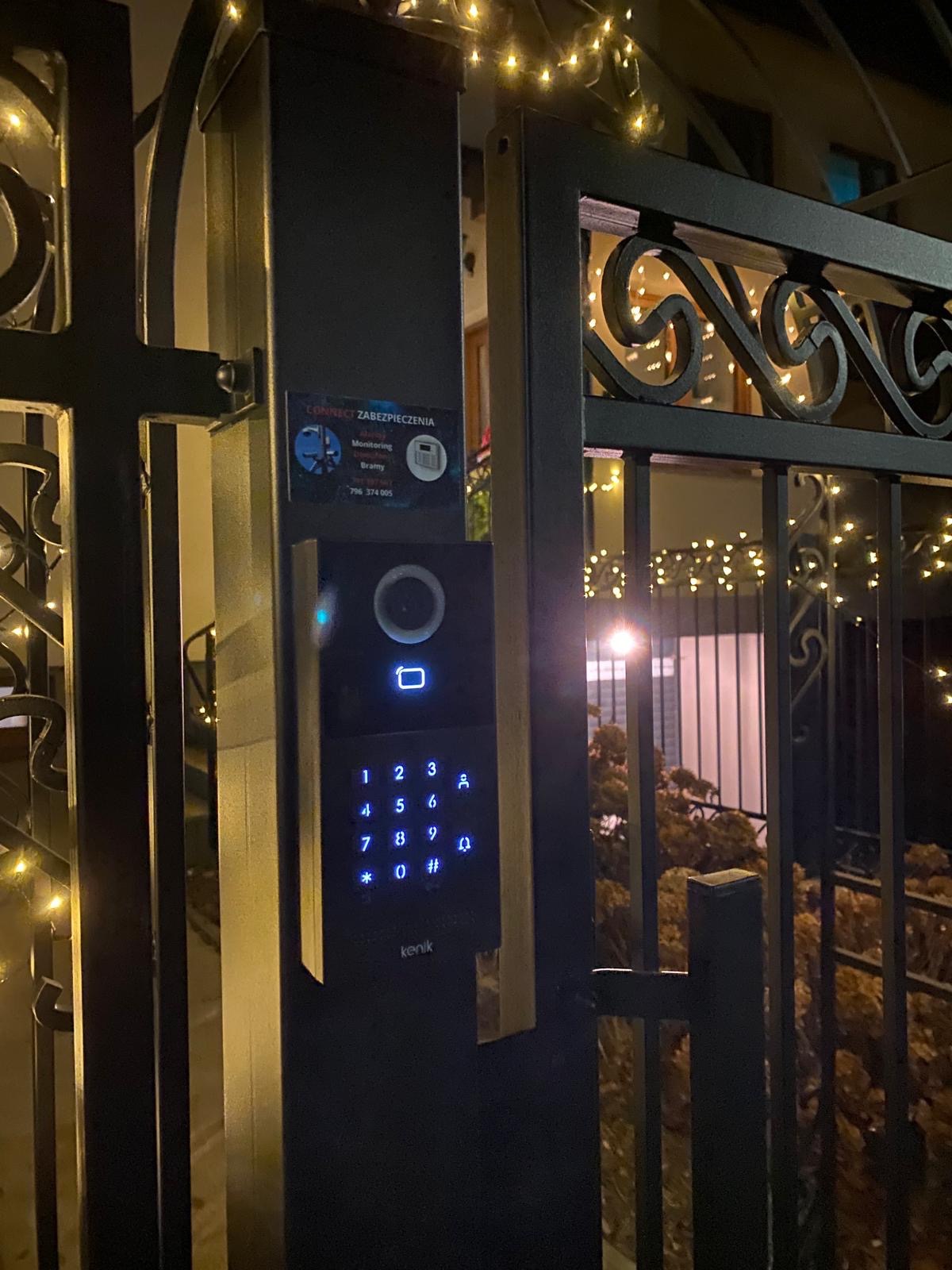 Nowoczesny wideodomofon Kenik z podświetlaną klawiaturą numeryczną, zamontowany na metalowej bramie wjazdowej, z widocznym logo firmy Connect Zabezpieczenia.