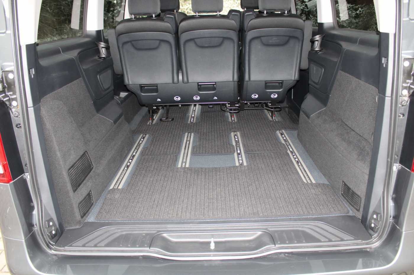 Wnętrze bagażnika szarego vana z trzema rzędami siedzeń i systemem szyn podłogowych do mocowania foteli.