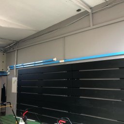 ULTECH Jakub Ulman - Klimatyzator kanałowy zamontowany przy suficie, z niebieską folią ochronną na kanałach wentylacyjnych, widoczna skrzynka elektryczna z symbolem ostrzegawczym.