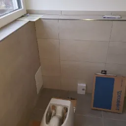 Montaż podwieszanej miski WC Duravit w łazience z beżowymi płytkami, widoczny karton i akcesoria montażowe.