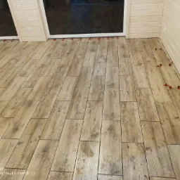 Układanie podłogowych płytek imitujących drewno w jasnym wnętrzu z użyciem czerwonych klipsów poziomujących.