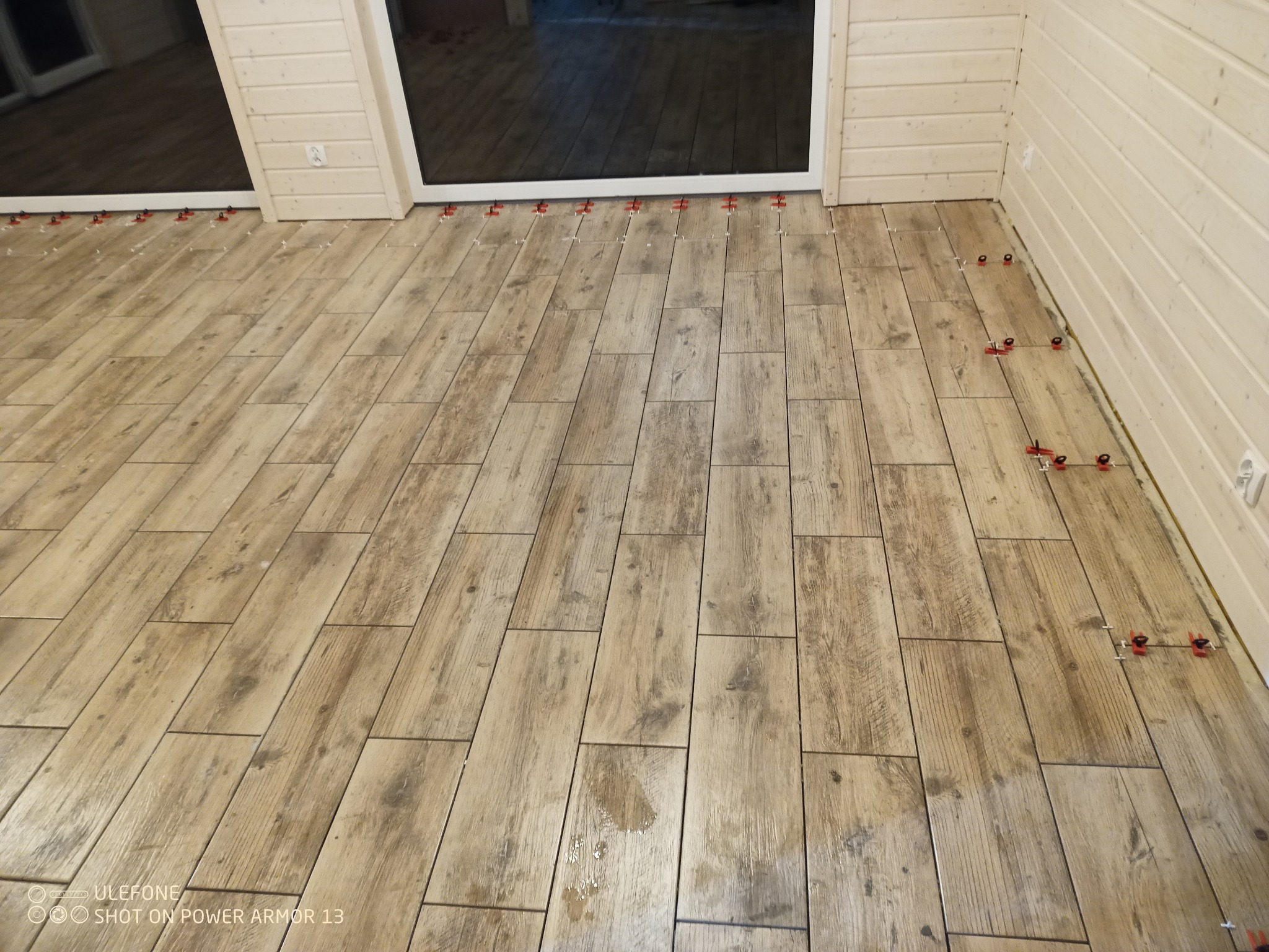 Układanie podłogowych płytek imitujących drewno w jasnym wnętrzu z użyciem czerwonych klipsów poziomujących.