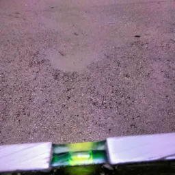 Poziomnica spoczywająca na nierównej powierzchni w trakcie wyrównywania, widoczne drobne nierówności i pył.