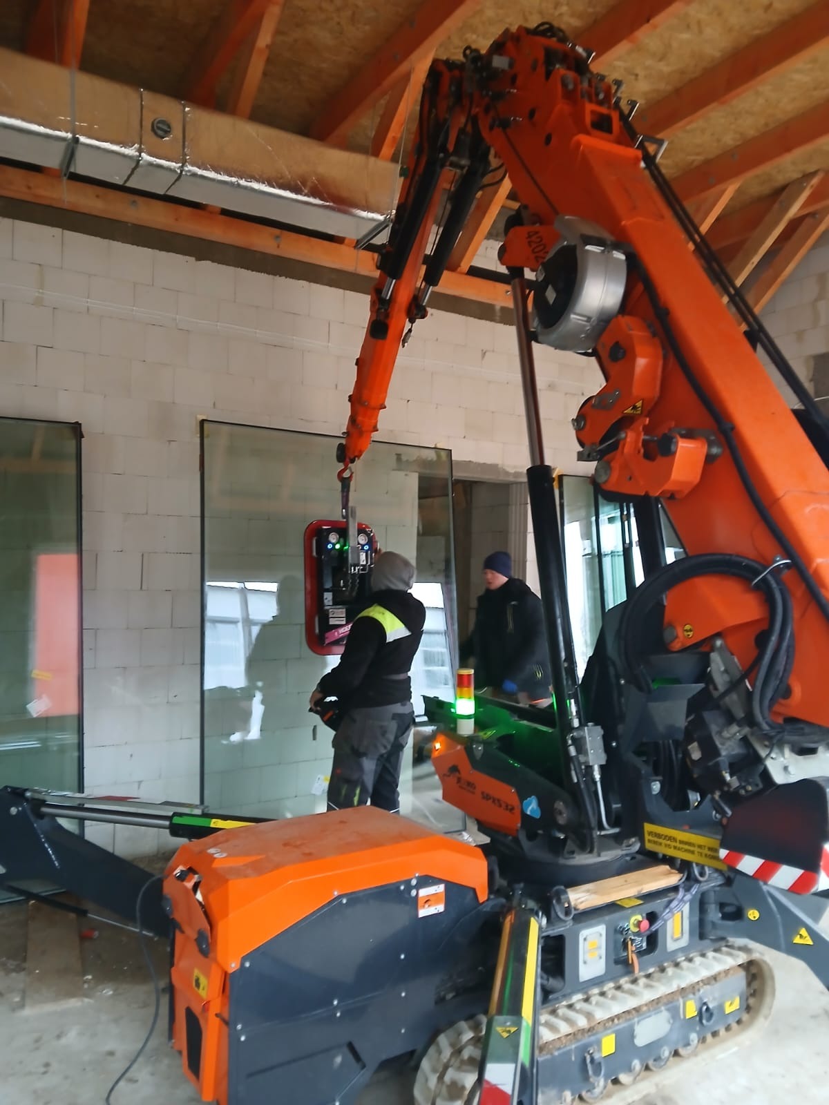 Montaż okien z użyciem specjalistycznego dźwigu przyssawkowego. Dwóch monterów nadzoruje proces, widoczne surowe mury budynku w trakcie budowy.