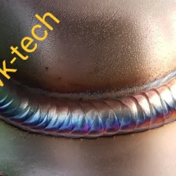 Szczegółowe zbliżenie na spaw wykonany metodą TIG, z widocznymi tęczowymi przebarwieniami termicznymi, ukazujące precyzję i jakość połączenia dwóch metalowych elementów.