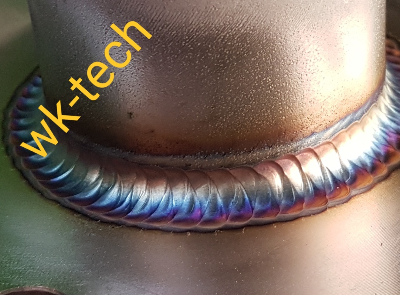 Szczegółowe zbliżenie na spaw wykonany metodą TIG, z widocznymi tęczowymi przebarwieniami termicznymi, ukazujące precyzję i jakość połączenia dwóch metalowych elementów.