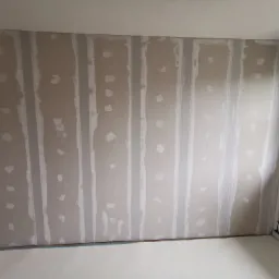 Ściana z płyt kartonowo-gipsowych ze szpachlowanymi łączeniami przed nałożeniem gładzi, zabezpieczona podłoga.