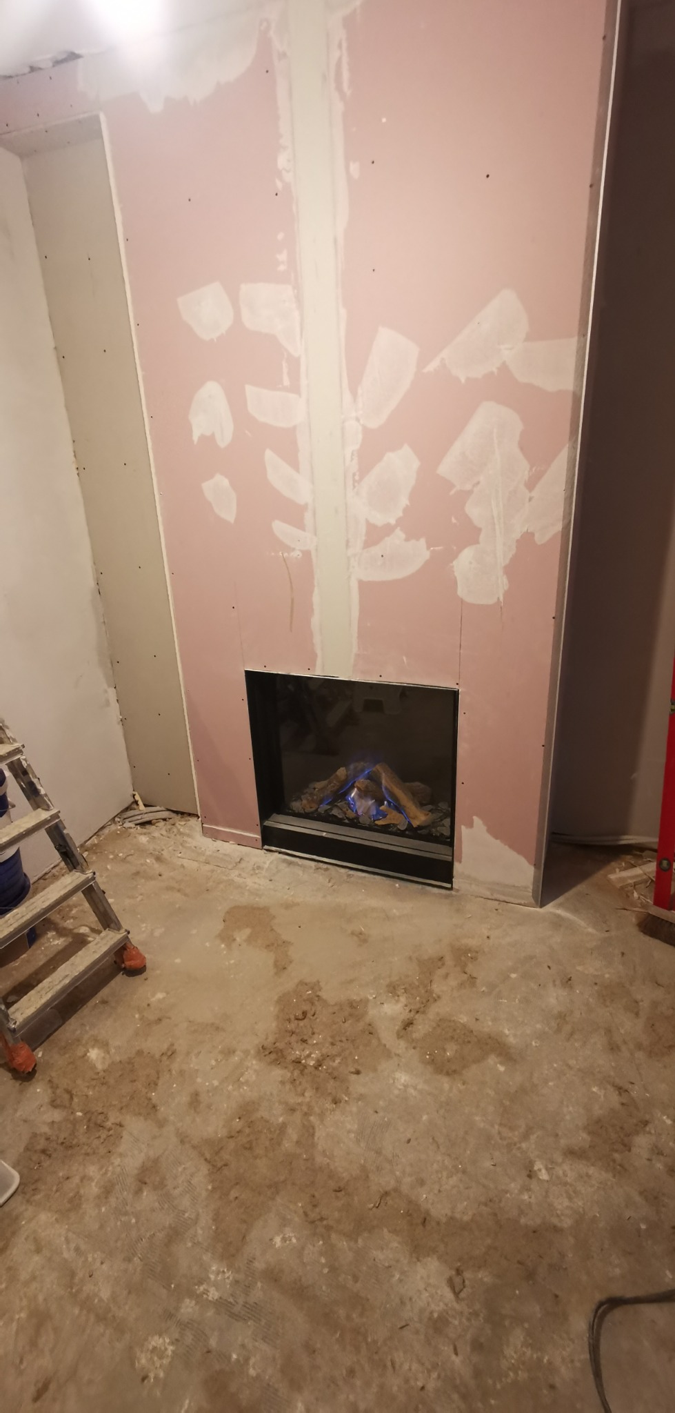 Montaż kominka elektrycznego z płyt karton-gips, widoczne ślady szpachlowania na różowej płycie, podłoga w trakcie remontu.