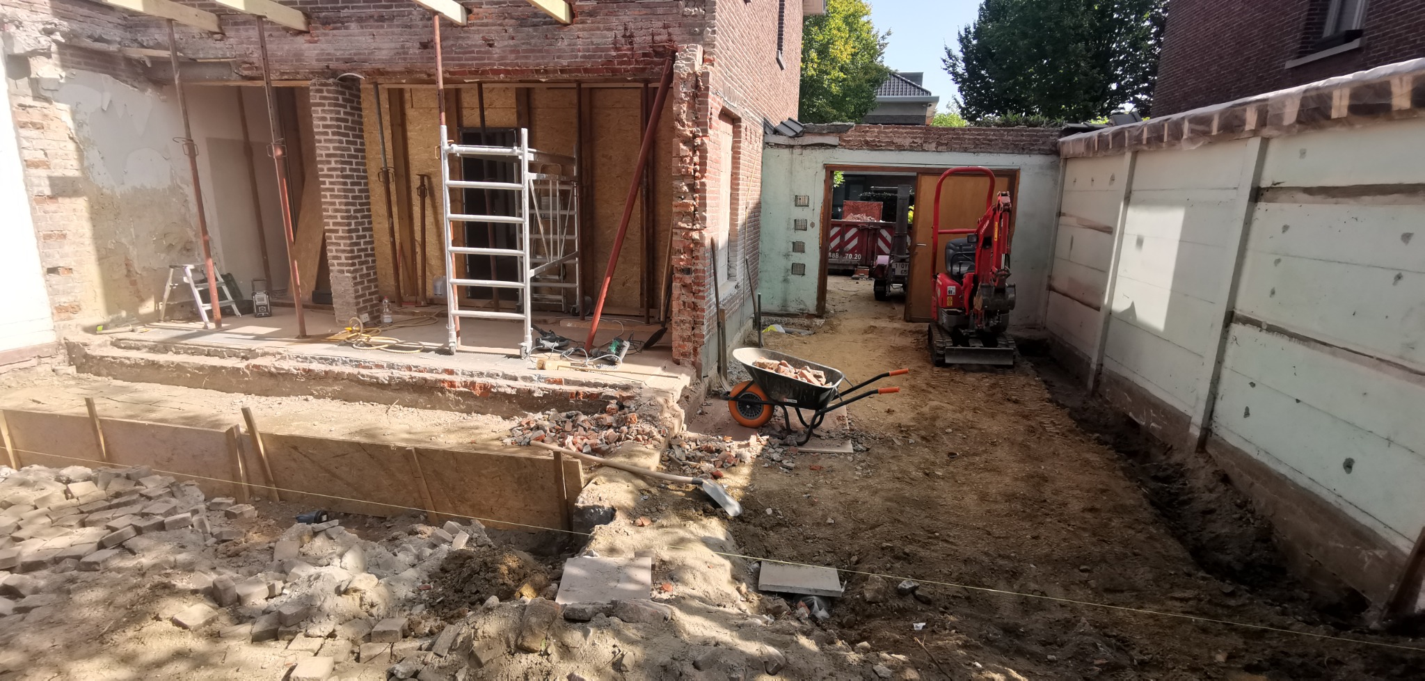 Przebudowa domu jednorodzinnego: widok na plac budowy z wykopem, rusztowaniem i minikoparką w tle.