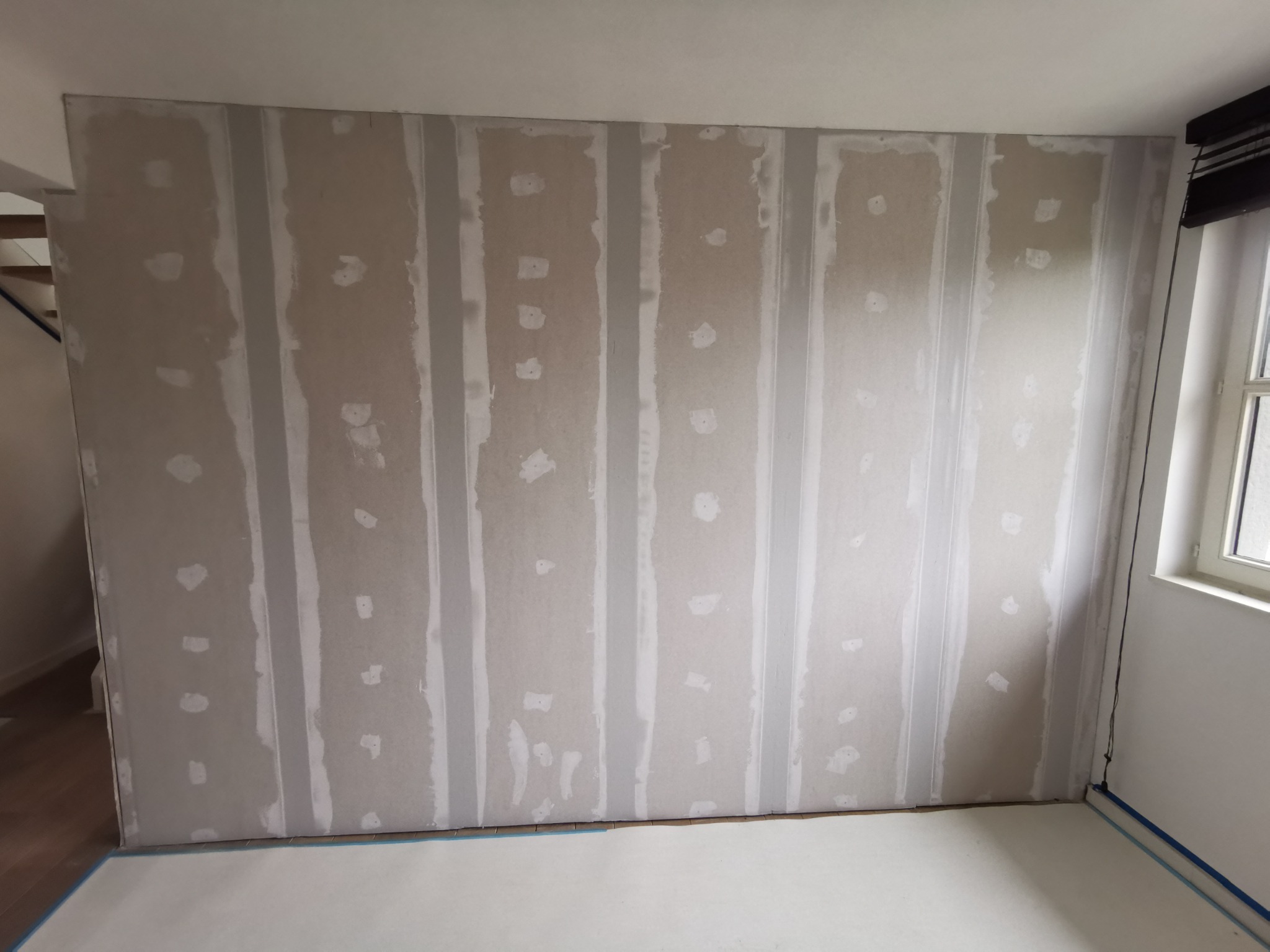 Ściana z płyt kartonowo-gipsowych ze szpachlowanymi łączeniami przed nałożeniem gładzi, zabezpieczona podłoga.