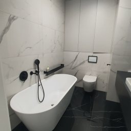 Usługi remontowe Krzysztof Dąbrowski - Nowoczesna łazienka w bieli i czerni: wolnostojąca wanna, marmurowe płytki ścienne i podłogowe, czarna armatura i minimalistyczne szafki.