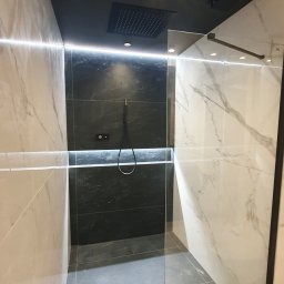 Usługi remontowe Krzysztof Dąbrowski - Nowoczesna kabina prysznicowa z czarną armaturą i marmurowymi płytkami, podświetlana listwą LED, tworząca elegancką strefę kąpieli.