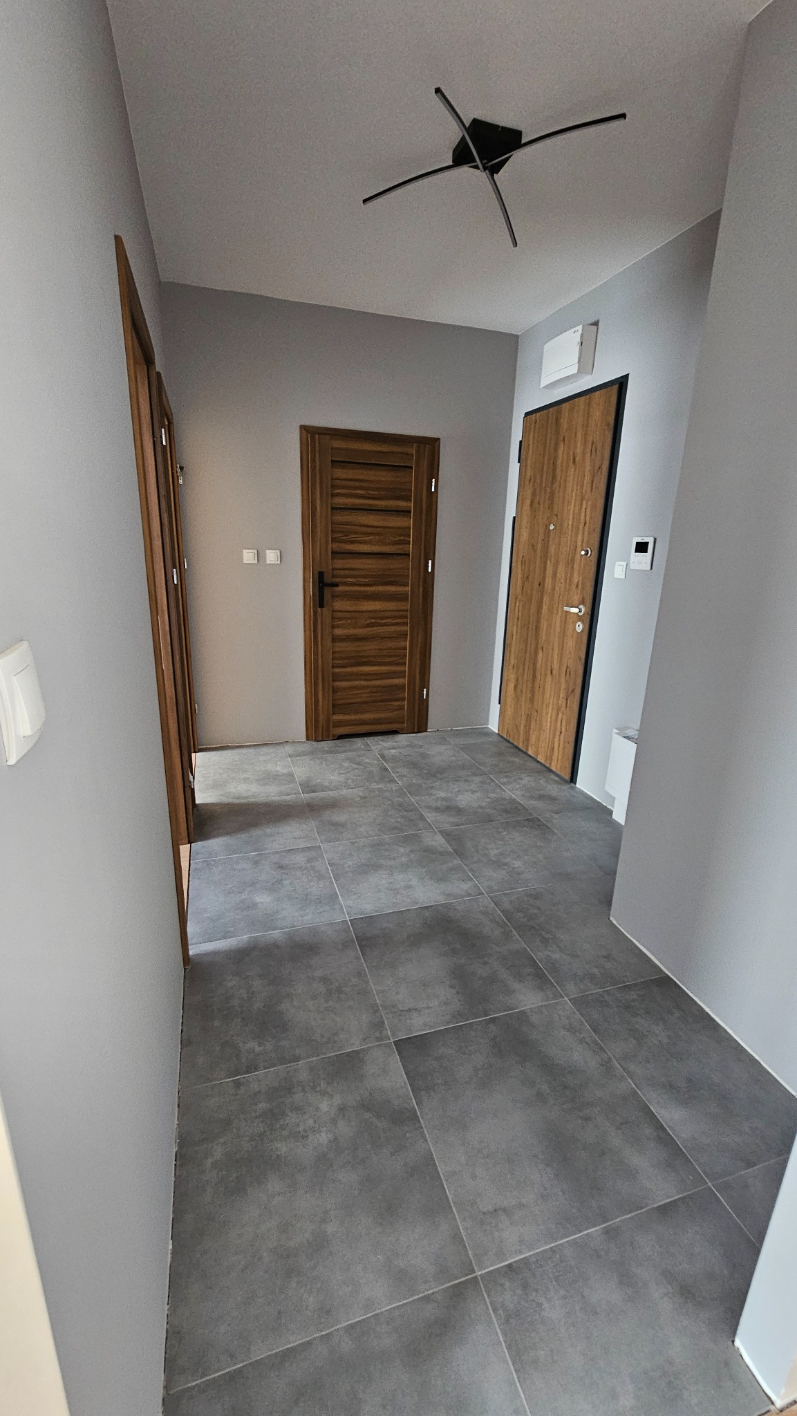 Szare płytki podłogowe w korytarzu, drewniane drzwi wewnętrzne i wejściowe. Nowoczesne wykończenie wnętrza w Poznań.