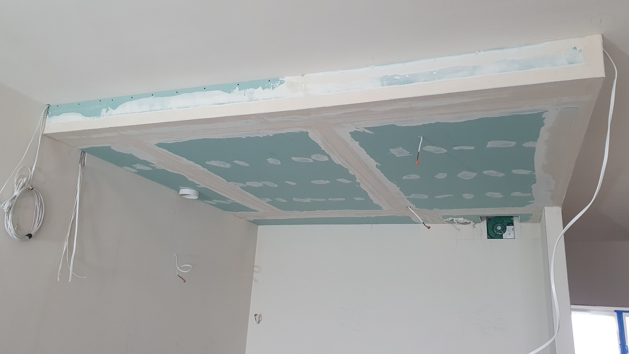 Sufit podwieszany z płyt karton-gips, częściowo zaszpachlowany, z widocznymi przewodami elektrycznymi i wentylacją. Etap prac wykończeniowych, surowy stan.