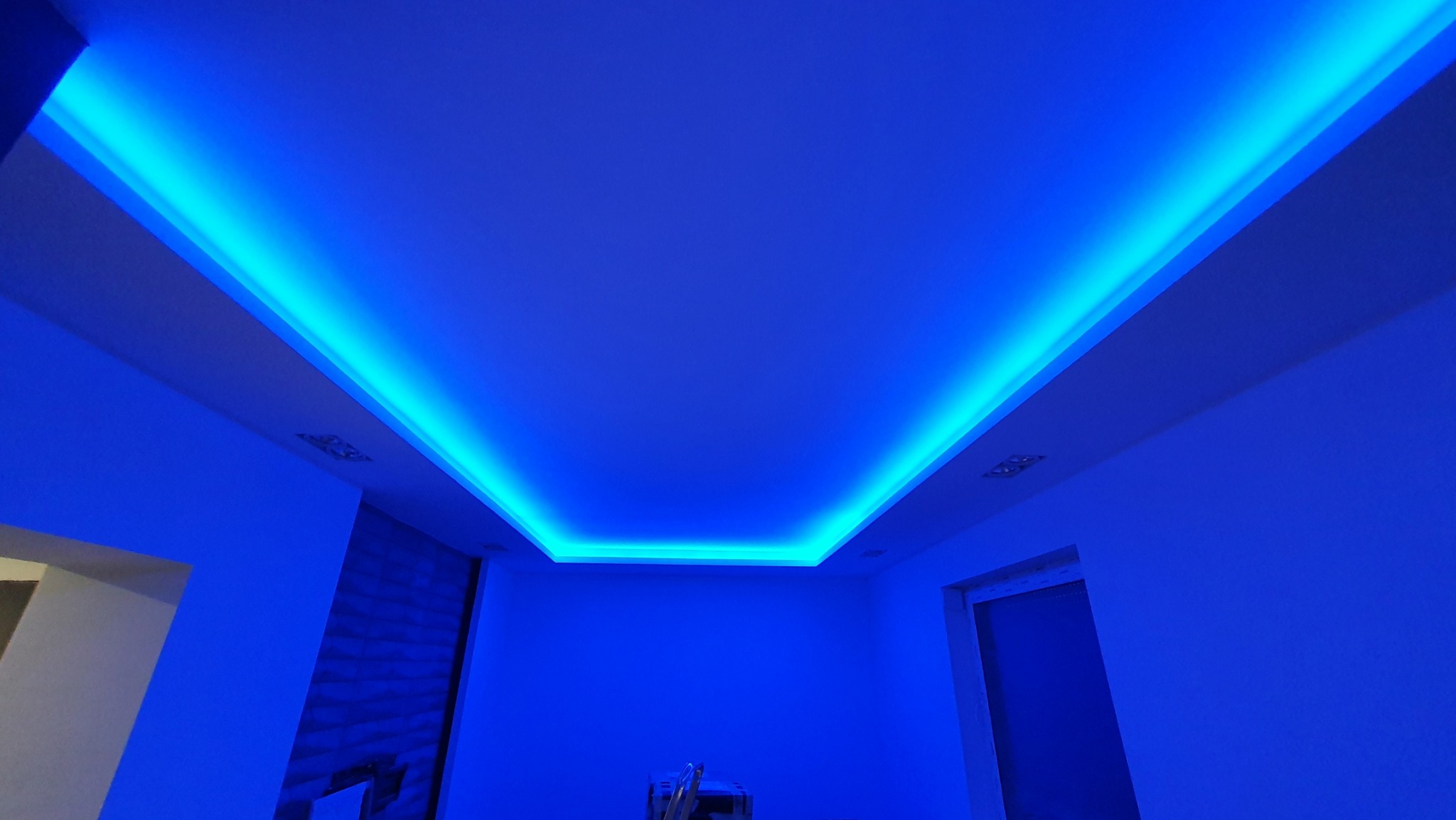 Podwieszany sufit z oświetleniem LED w kolorze niebieskim, tworzący nowoczesny i nastrojowy klimat w pomieszczeniu. Widoczne detale wykończenia ścian i sufitu.