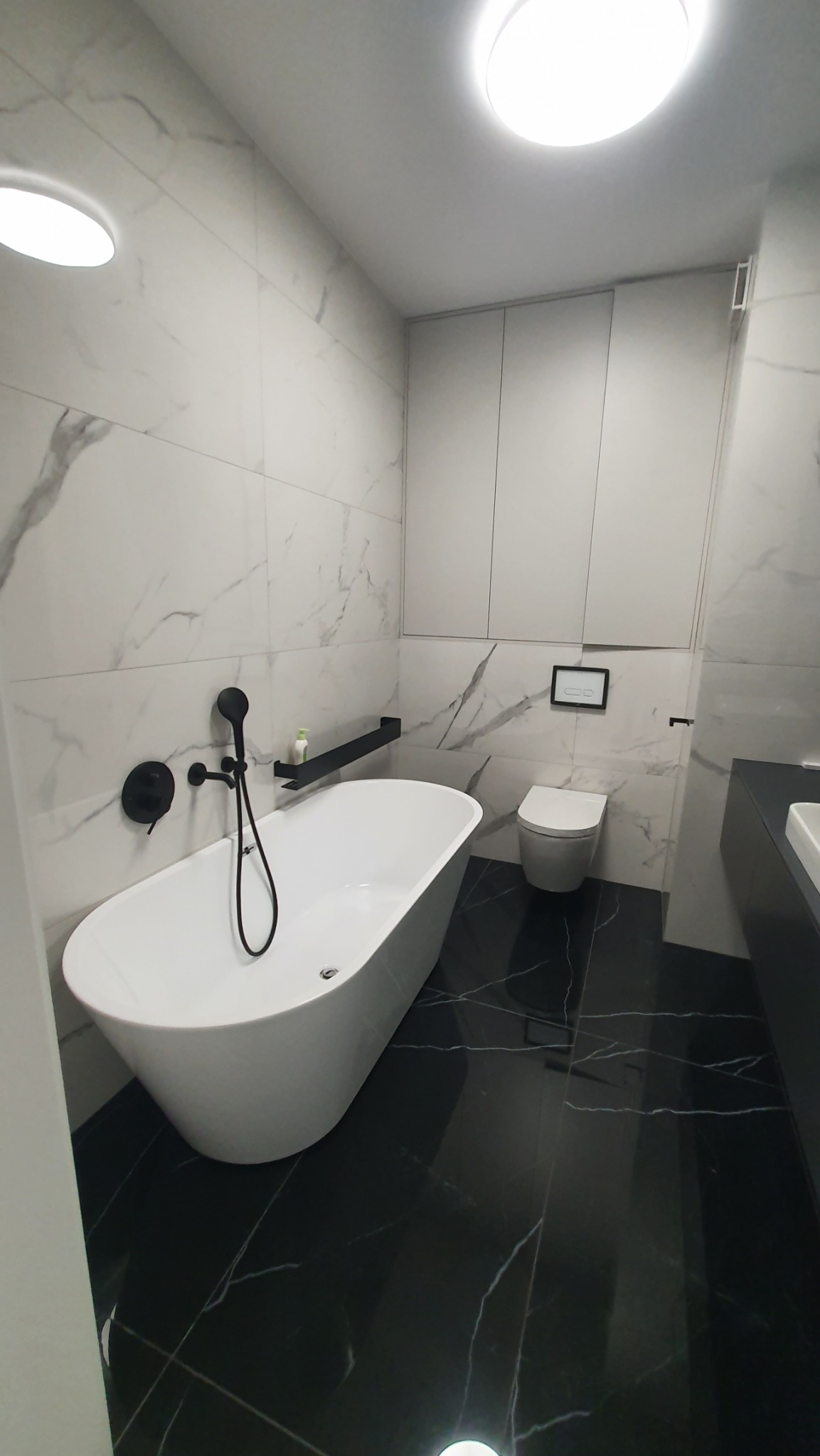 Nowoczesna łazienka w bieli i czerni: wolnostojąca wanna, marmurowe płytki ścienne i podłogowe, czarna armatura i minimalistyczne szafki.