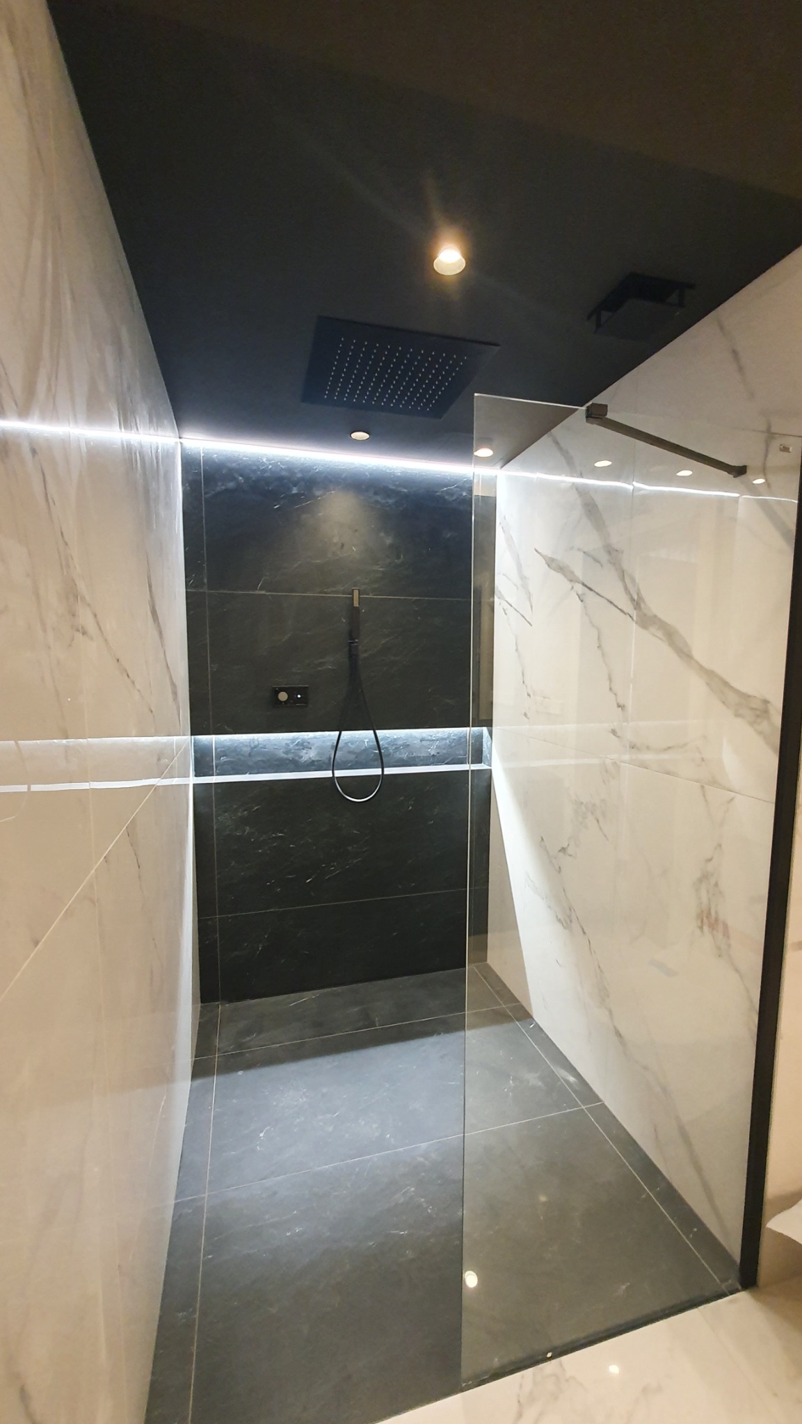 Nowoczesna kabina prysznicowa z czarną armaturą i marmurowymi płytkami, podświetlana listwą LED, tworząca elegancką strefę kąpieli.