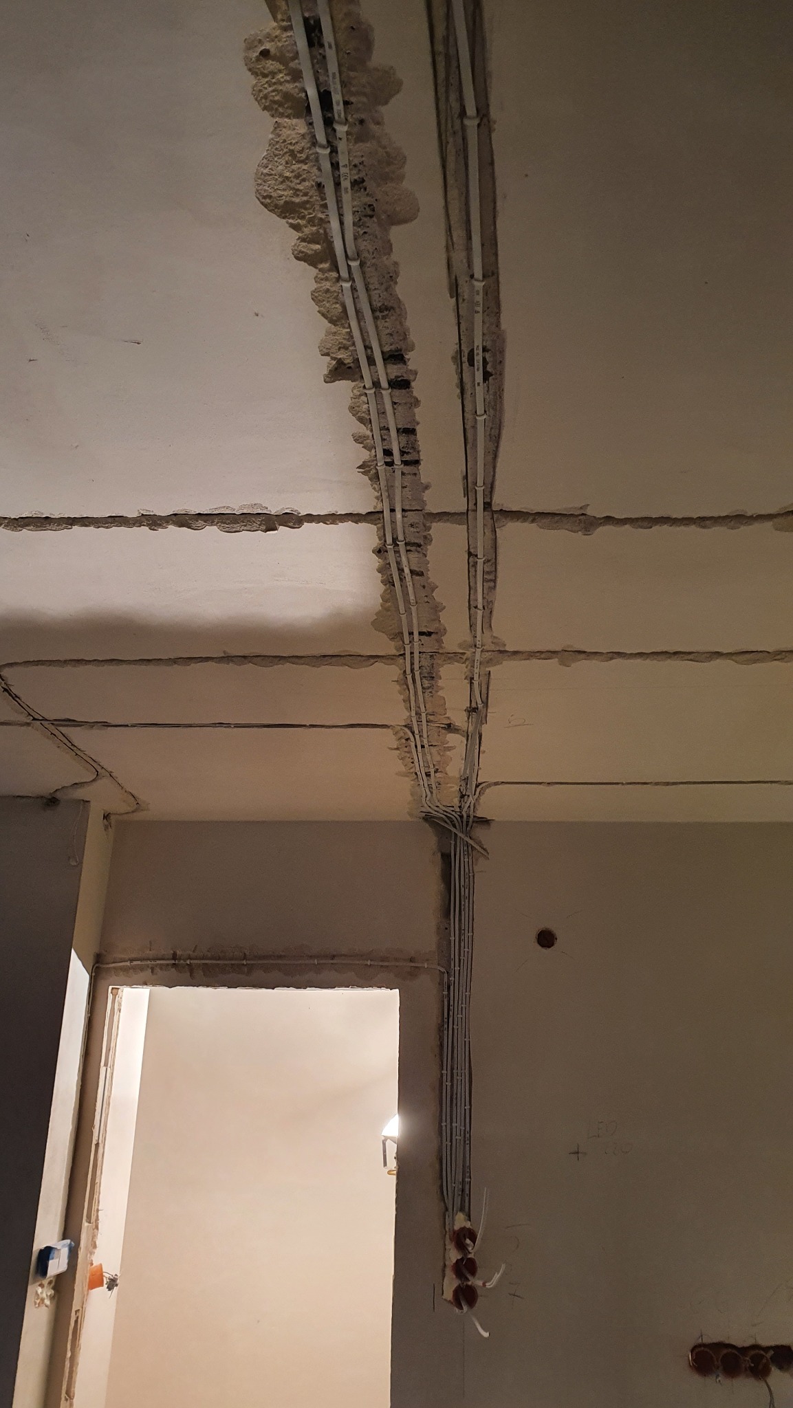 Instalacja elektryczna w bruzdach sufitu i ściany, widoczne przewody i puszki. Przygotowanie do tynkowania, surowy stan wykończenia wnętrza.