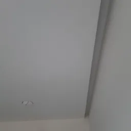 Wnętrze w trakcie prac wykończeniowych: pomalowany sufit z przygotowanym otworem na oświetlenie, zabezpieczone kable na ścianie, widoczna listwa przypodłogowa.