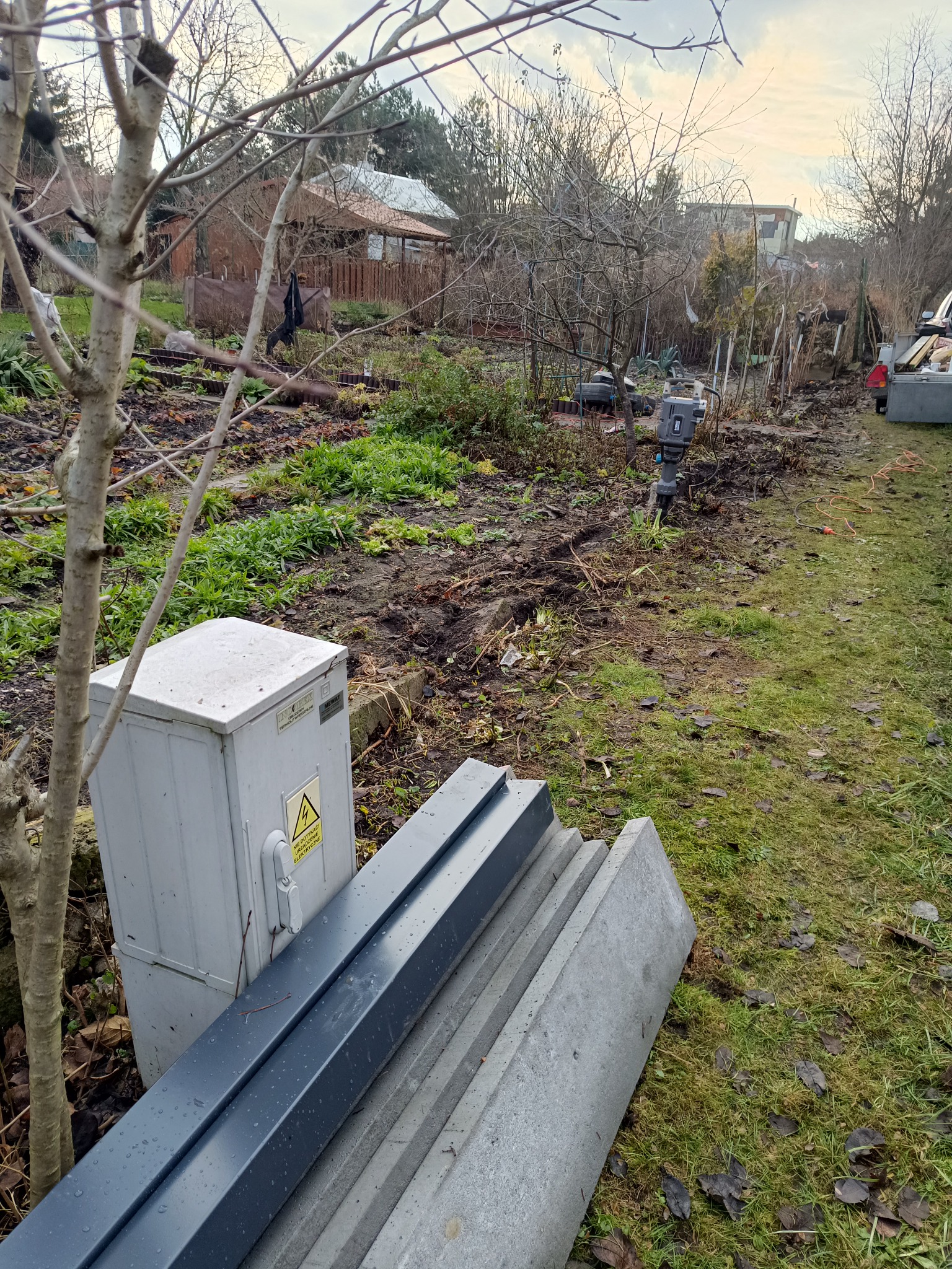 Przygotowanie terenu pod montaż ogrodzenia w miejscowości Dobre: widoczne słupki i podmurówka ogrodzeniowa, ubijarka do gruntu oraz skrzynka elektryczna.