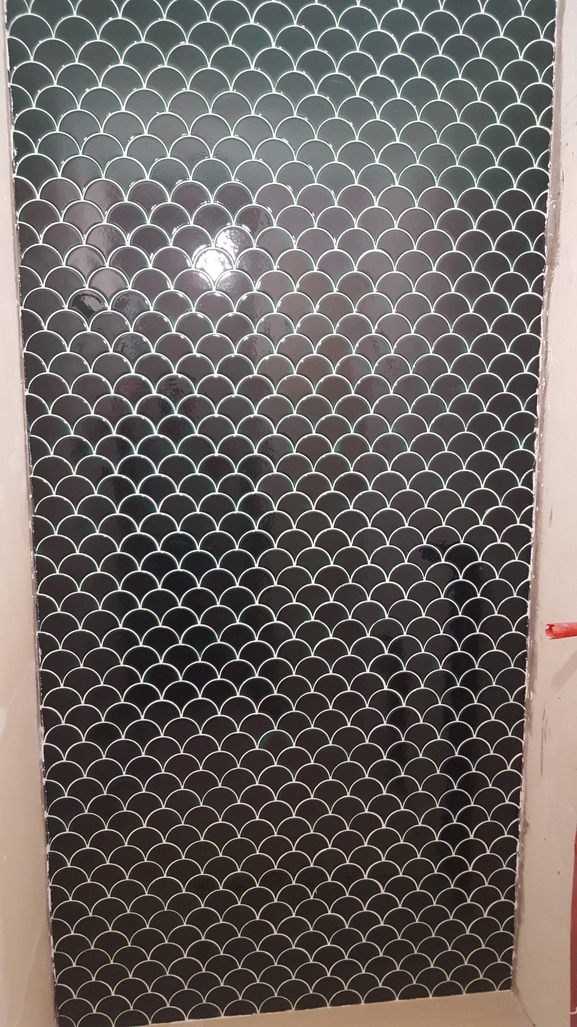 Ściana wyłożona błyszczącymi, czarnymi płytkami w kształcie rybiej łuski z białą fugą, wykonana w Gdańsku.