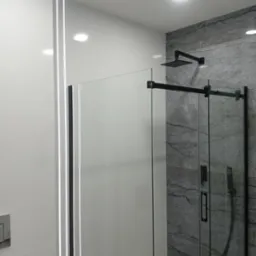 Nowoczesna kabina prysznicowa z czarnymi elementami, podświetlana listwa LED wzdłuż ściany, szara marmurowa okładzina.