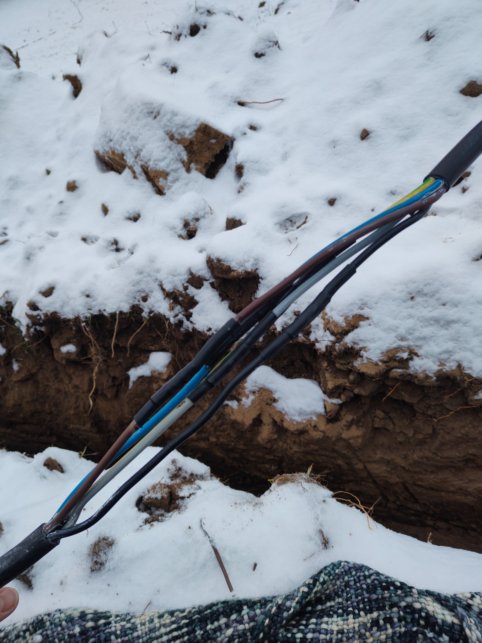 Kabel elektryczny z kolorowymi żyłami wystający z ziemi pokrytej śniegiem, widoczne łączenia izolacyjne.